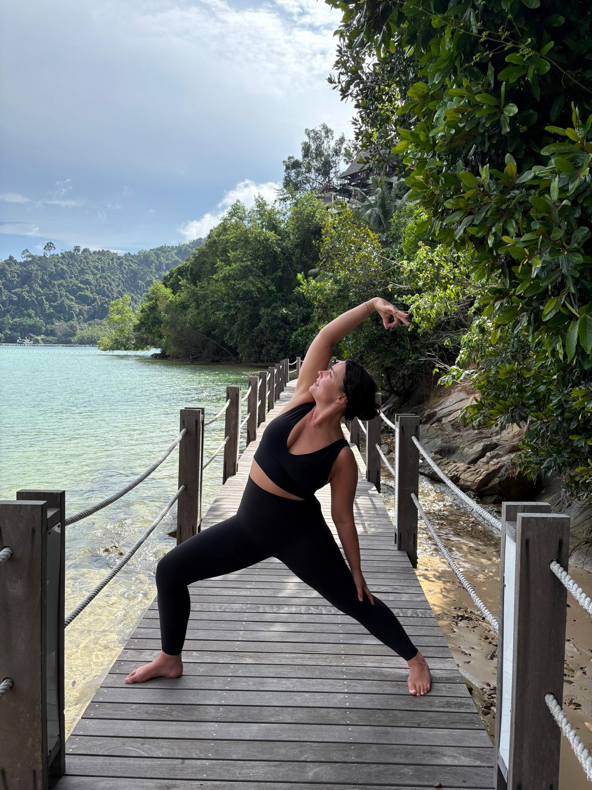 Clare in a side stretch on a wooden boardwalk by the water.
