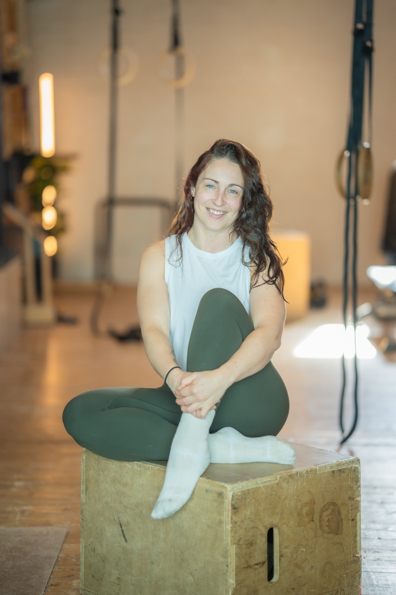 Maria sitting on a wooden box in a studio, smiling.